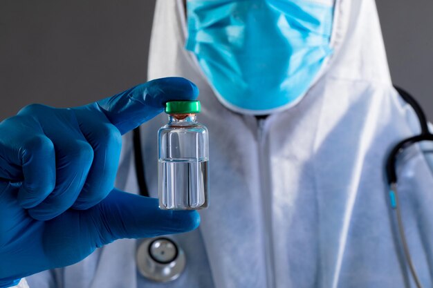 Mid section of health worker wearing protective clothes holding covid-19 vaccine bottle