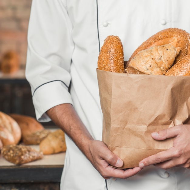 Photo mid section of maker holding baked breads in paper bag