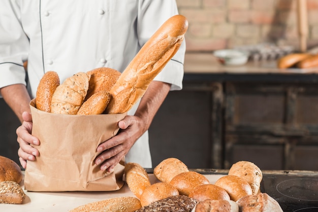 Foto metà di sezione del panettiere maschio che tiene sacchetto di carta con diversi tipi di pane