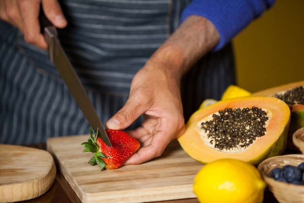 Mid-section of male staff cutting strawberry at organic section