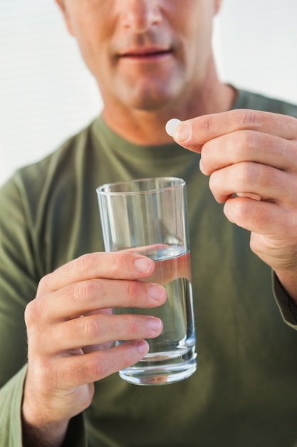 Mid section of a man holding glass of water and pill