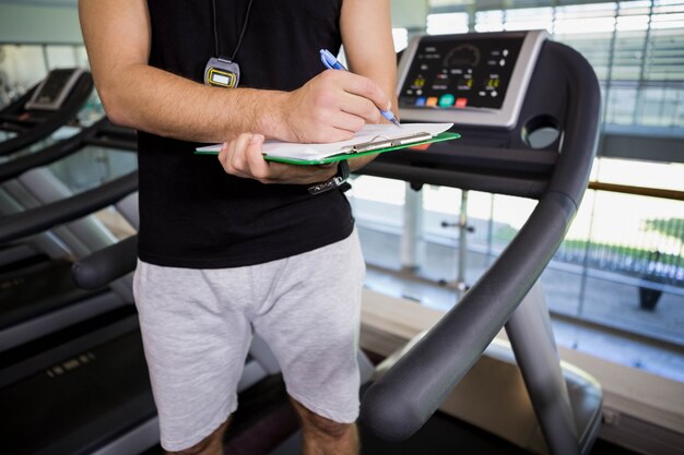 Mid section of man on treadmill writing on clipboard at the gym