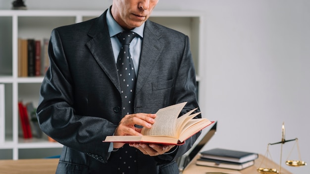 Photo mid section of mature lawyer reading book in the office