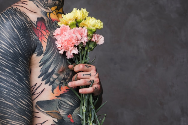 Фото Средняя часть татуированного молодого человека без рубашки, держащего гвоздику в руках