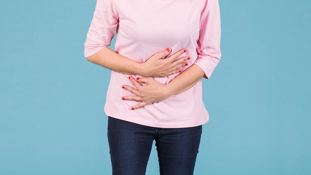Фото Средняя часть женщины с боли в животе, стоя на синем фоне