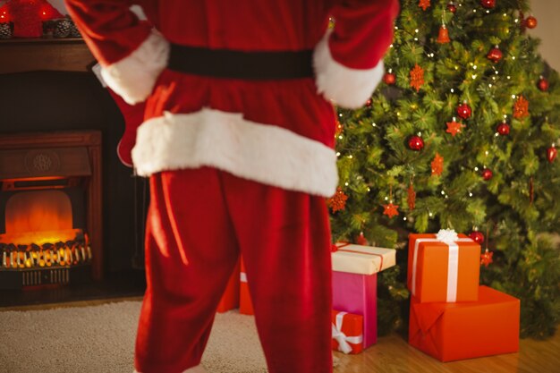 Mid section of santa standing in front of the christmas tree