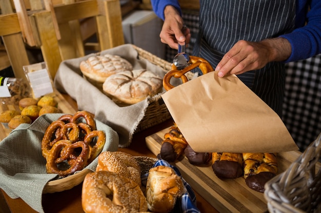 Mid section of staff packing croissant in paper bag at counter