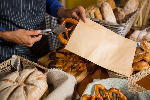 Mid section of staff packing pretzel bread in paper bag at counter