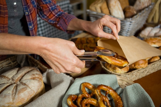 Mid section of staff packing pretzel bread in paper bag at counter