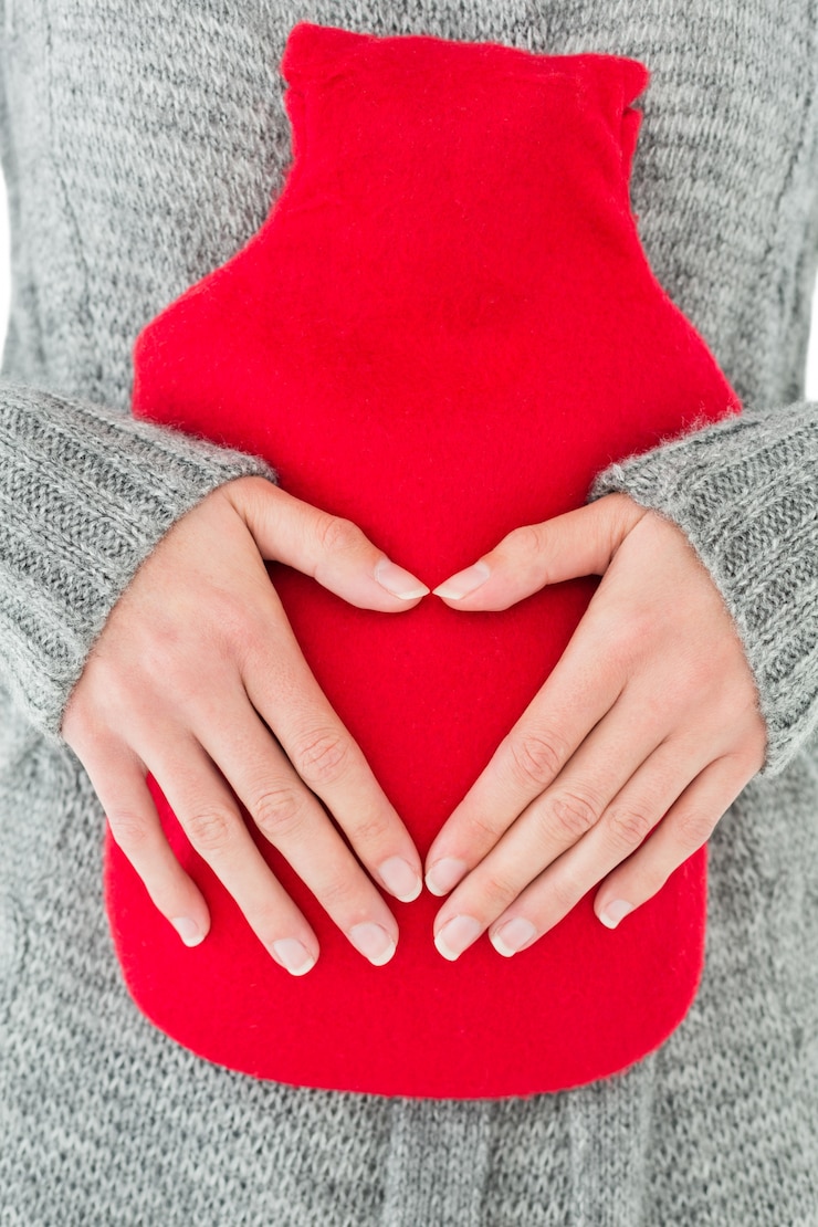 Photo mid section of a woman holding red hot water bag on abdomen