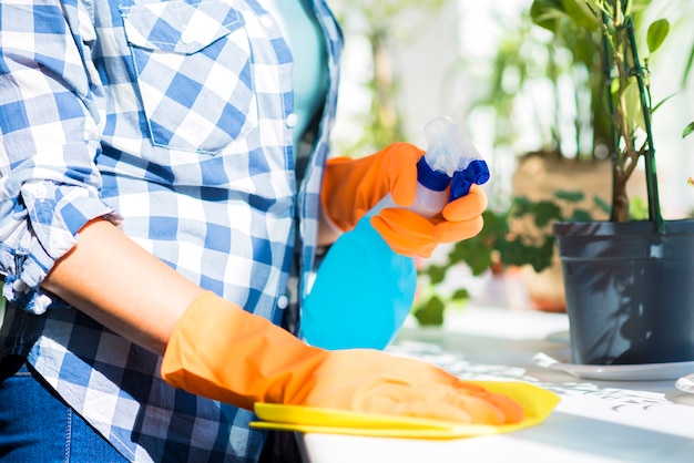 Foto metà di sezione della mano della donna che pulisce la superficie bianca con spray disinfettante