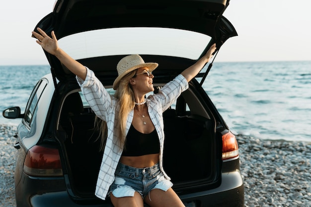 Foto metà di colpo donna felice in piedi nel bagagliaio di un'auto con bottiglia di succo