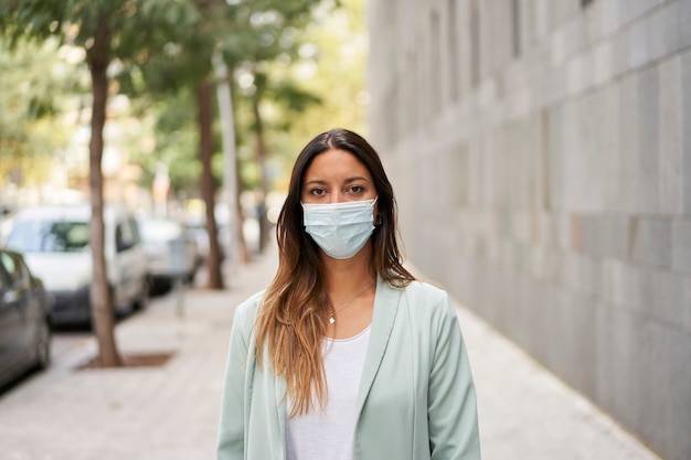 Mid shot van een werkende vrouw in de stad met een masker voor de coronavirus pandemie. Ze staat voor de camera.