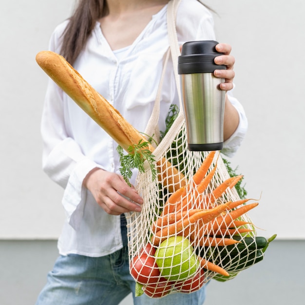 mid shot woman and holding reusable bag and thermos outside