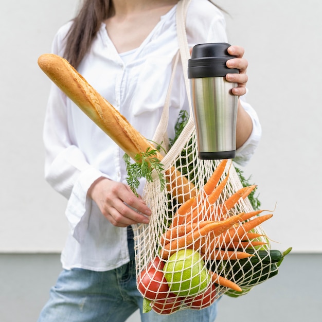 Photo mid shot woman and holding reusable bag and thermos outside