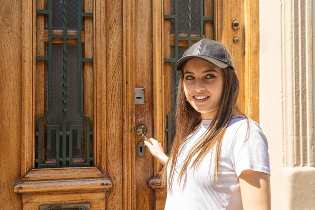 Mid shot of a Young Hispanic woman opening an old wooden door of a house to enter.