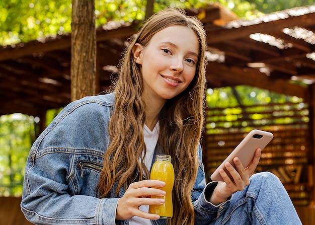 Середина выстрела молодая женщина, держащая бутылку свежего сока и телефон