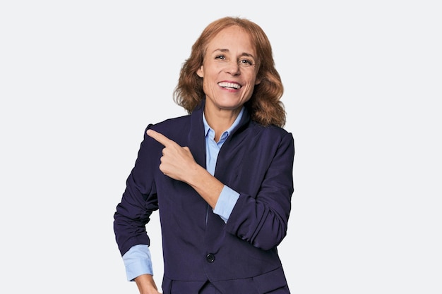 Photo midaged caucasian businesswoman in blazer smiling and pointing aside showing something