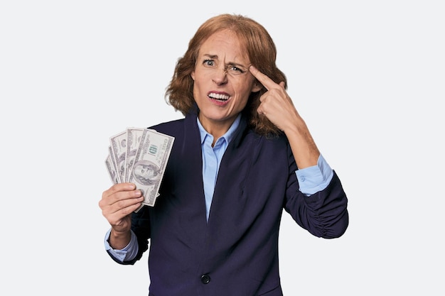 Photo midaged caucasian with dollars in studio showing a disappointment gesture with forefinger