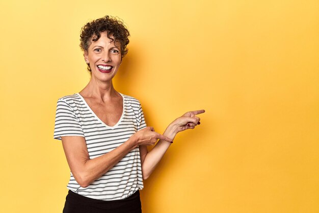 Midaged caucasian woman on vibrant yellow excited pointing with forefingers away
