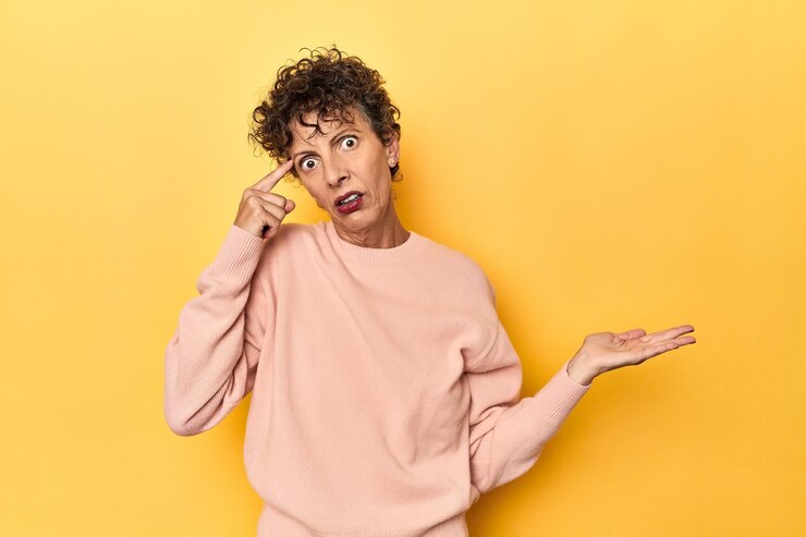 Photo midaged caucasian woman on vibrant yellow holding and showing a product on hand