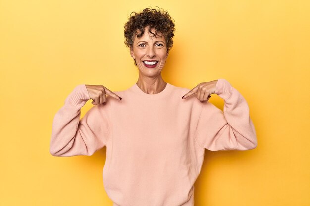 Midaged caucasian woman on vibrant yellow surprised pointing with finger smiling broadly