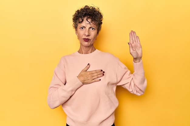 Midaged caucasian woman on vibrant yellow taking an oath putting hand on chest