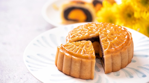 MidAutumn Festival traditional food concept Beautiful cut moon cake on blue pattern plate on white background with flower close up copy space