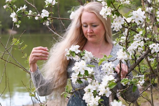 Middel aged woman stands in the park next to a flowering tree spring time