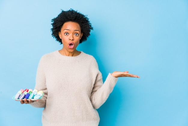 Middelbare leeftijd Afro-Amerikaanse vrouw eten bitterkoekjes geïsoleerd onder de indruk kopie ruimte op palm te houden.