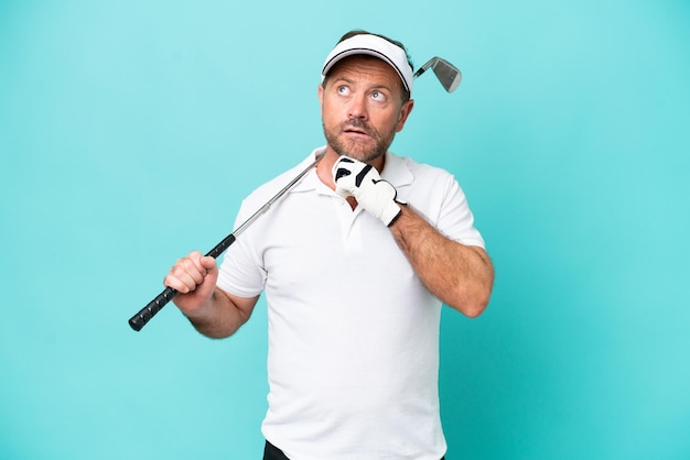 Middelbare leeftijd blanke golfer speler man geïsoleerd op blauwe achtergrond en omhoog kijkend