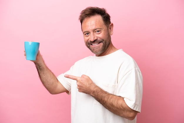 Middelbare leeftijd blanke man met kopje koffie geïsoleerd op roze achtergrond en wijzend