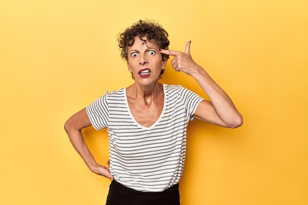 Middelbare leeftijd blanke vrouw op levendig geel met een teleurstellingsgebaar met wijsvinger