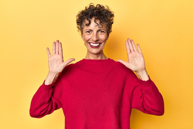 Foto middelbare leeftijd blanke vrouw op levendig geel met nummer tien met handen