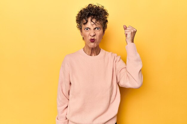 Foto middelbare leeftijd blanke vrouw op levendig geel met vuist naar camera agressieve gezichtsuitdrukking