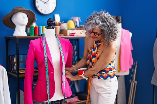 Middelbare leeftijd grijsharige vrouw kleermaker glimlachend zelfverzekerd meetjasje in naaiatelier