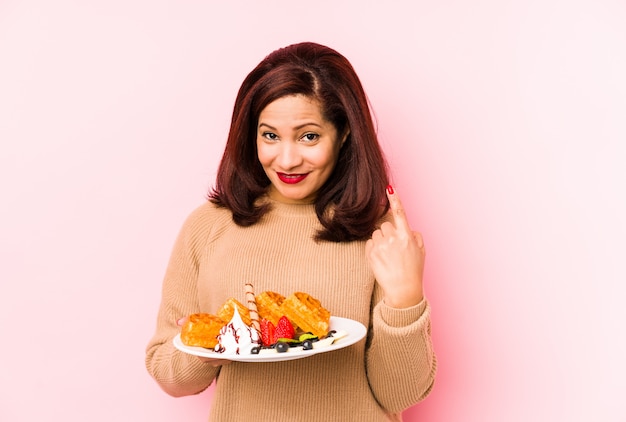 Middelbare leeftijd Latijnse vrouw met een wafel geïsoleerd wijzend met vinger naar je alsof uitnodigen dichterbij komen.