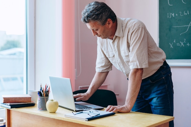 Middelbare leeftijd leraar leunde naar laptop nad typen.