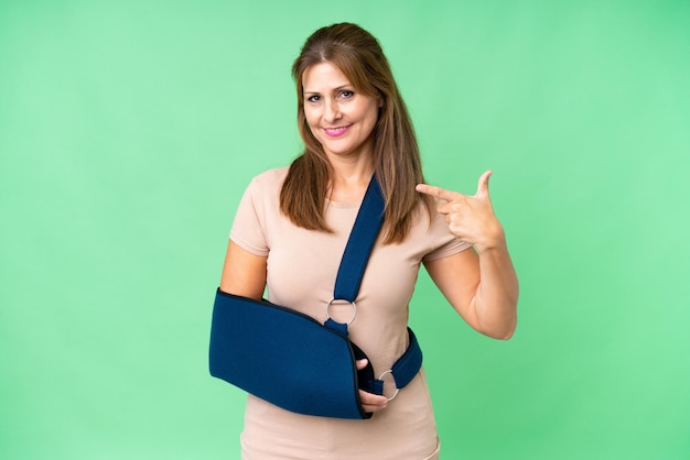Middelbare leeftijd met gebroken arm en het dragen van een mitella over geïsoleerde achtergrond met een duim omhoog gebaar