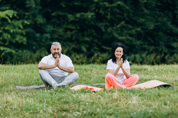 Middelbare leeftijd vrouw en man doen yoga samen buitenshuis gebaar maken namaste.