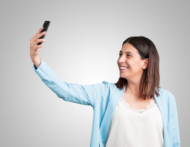 Middelbare leeftijd vrouw zelfverzekerd en vrolijk, het nemen van een selfie, kijkend naar de mobiel met een grappige en zorgeloze gebaar, surfen op de sociale netwerken en internet
