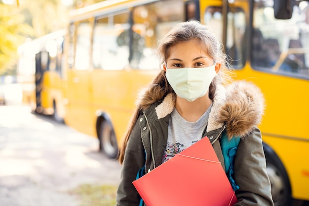 Middelbare schoolmeisjesleerling met beschermend masker voor schoolbus klaar om met de bus naar huis te gaan