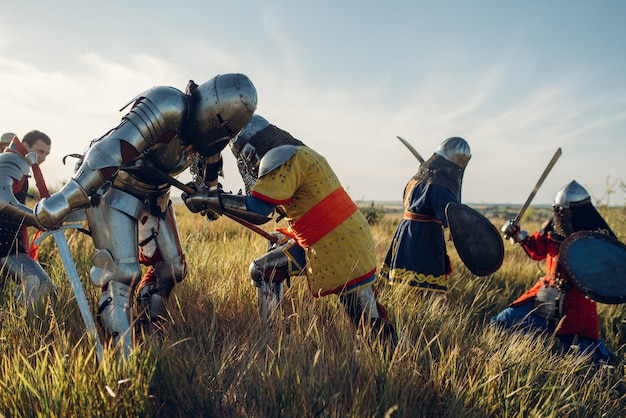 Middeleeuwse ridders in harnassen en helmen vechten met zwaard en bijl, grote strijd. gepantserde oude krijger in pantser poseren in het veld