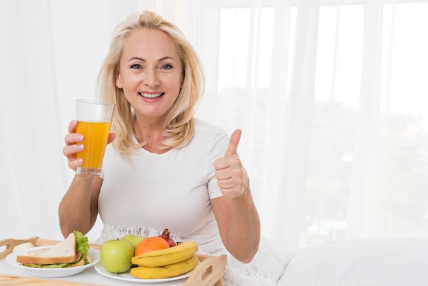 Middelgrote geschotene gelukkige vrouw met jus d'orange die goedkeuring toont