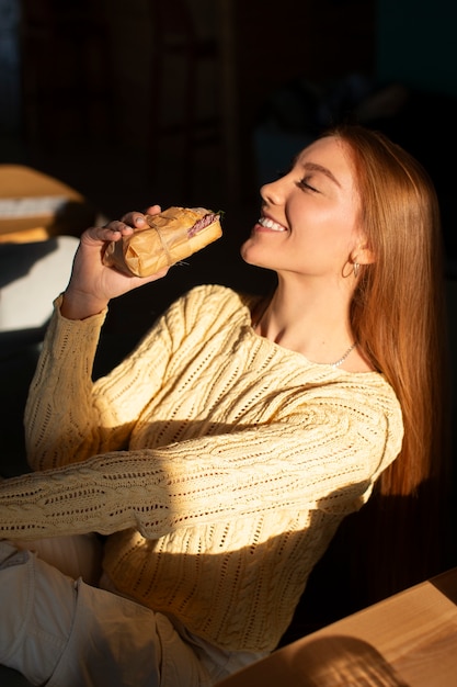 Foto middelgrote vrouw met een in papier gewikkeld broodje.