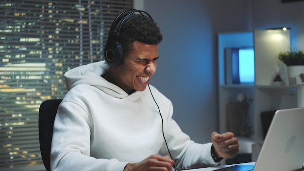 Middellange schot van Afrikaanse gamer in hoofdtelefoons die online spel op computer winnen