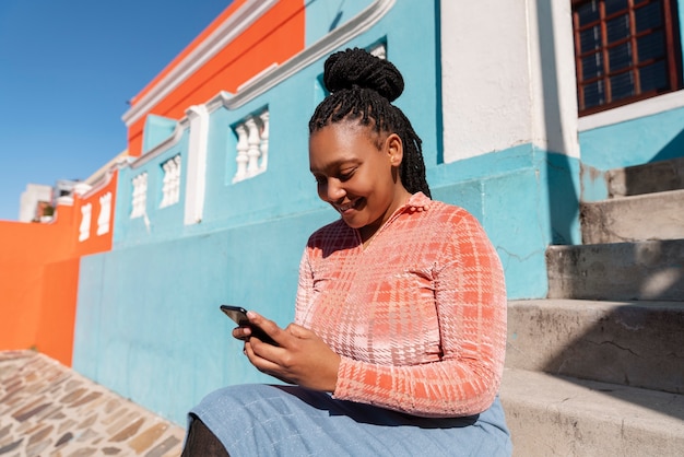 Middellange shot vrouw die smartphone buitenshuis gebruikt