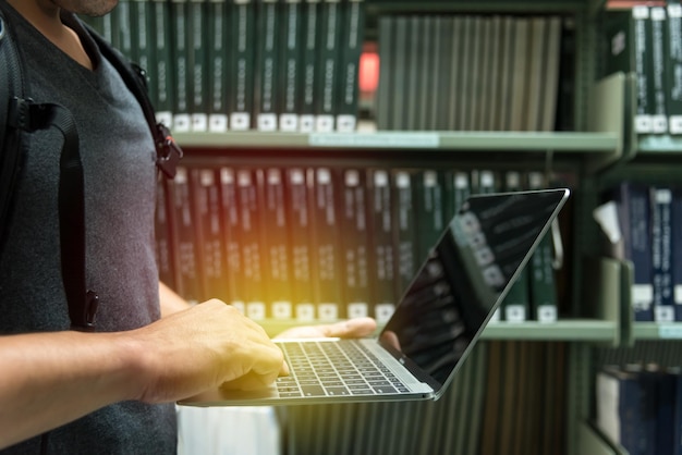 Middels sectie van een mannelijke student die een laptop gebruikt in de bibliotheek