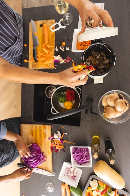 Foto middelsectie van een diverse koppel die maaltijden bereiden, groenten hakken en afval in de keuken composteren. voedsel, koken, samenleven, relatie, ecologie, recycling, levensstijl en huishoudelijk leven.