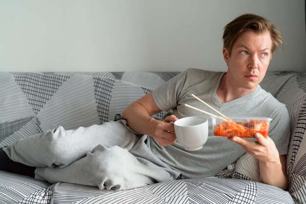 Foto middelsectie van een man die koffie vasthoudt terwijl hij thuis op de bank zit